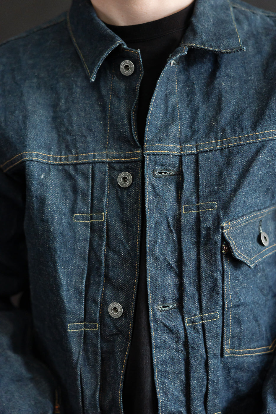 Close-up front view of 15oz selvedge denim jacket on male model, showing buttons, collar, and chest pocket. Model is 5'9