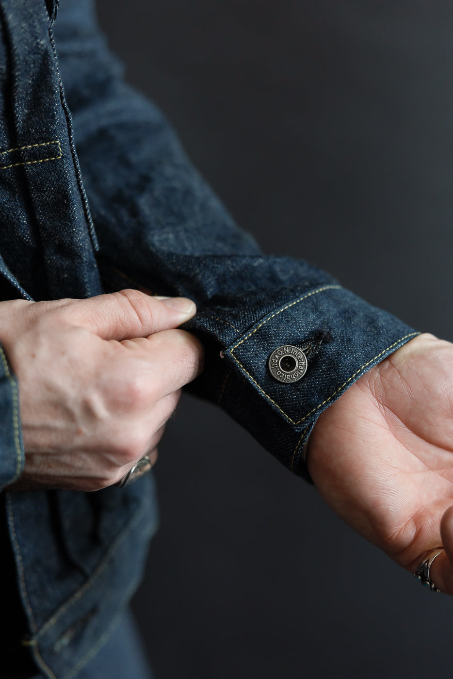 Close-up of male model adjusting cuff on selvedge denim jacket sleeve, showing button detail