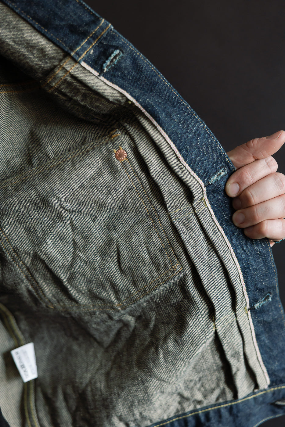 Close-up of inside front selvedge denim jacket showing inner pocket, stitching, and fabric texture.