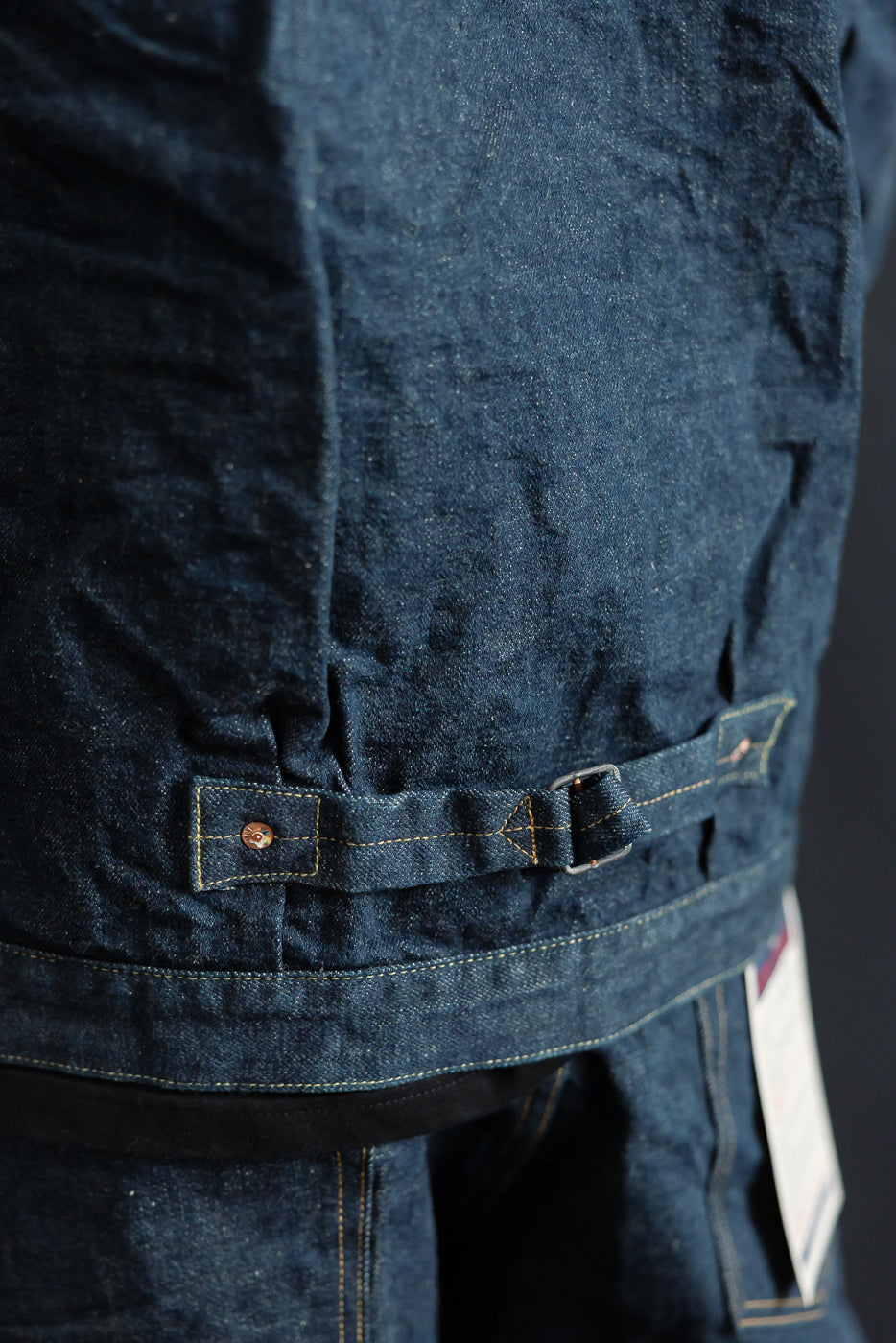 Close-up of the back waist cinch and stitching details on a men's selvedge denim jacket.
