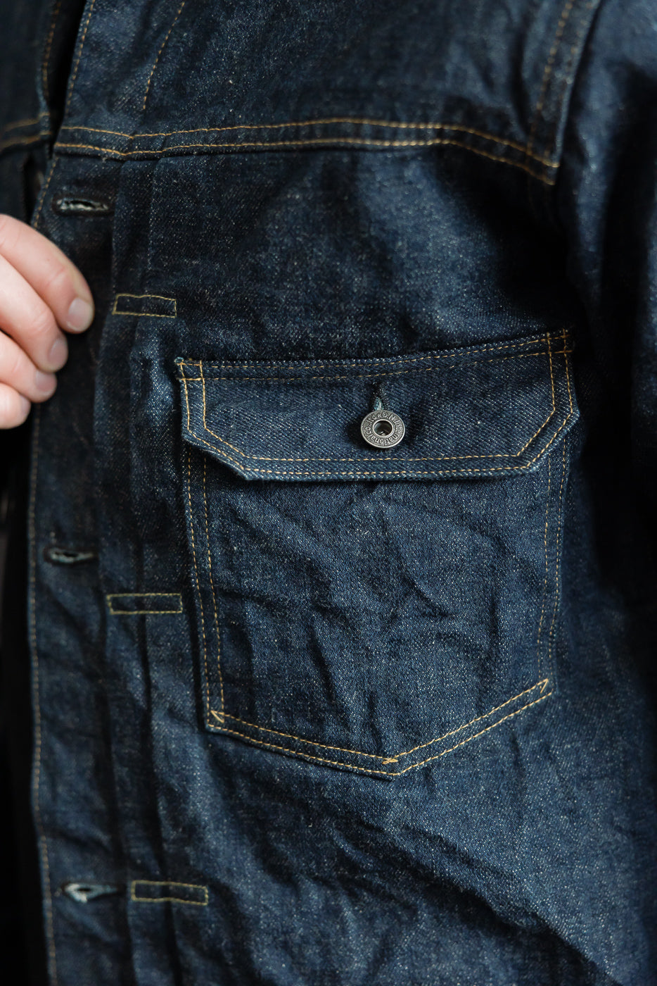 Close-up of front chest pocket and button on 15oz selvedge denim jacket, male model 5'9 165lbs athletic build