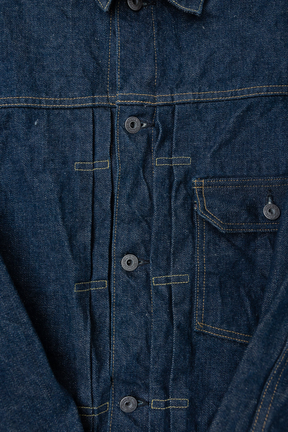 Close-up of front chest area on selvedge denim jacket, showing buttons, pocket, and stitching details.