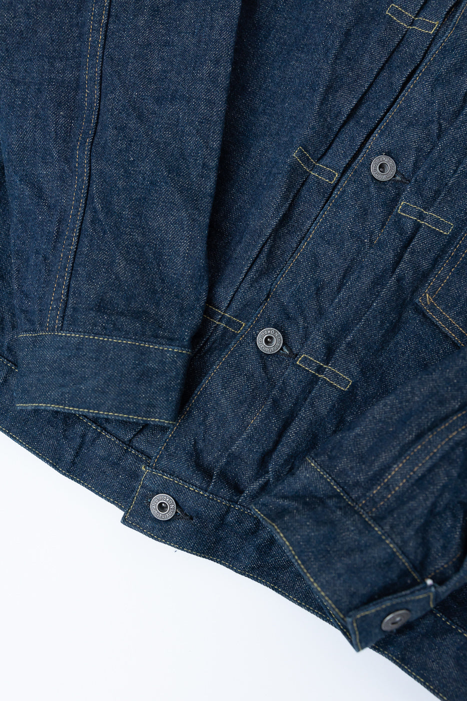 Close-up of front hem and buttons on selvedge denim jacket, showing texture and stitching.