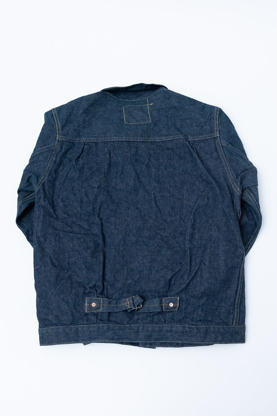 Flat lay of back side of selvedge denim jacket, showing rear cinch and stitching details.