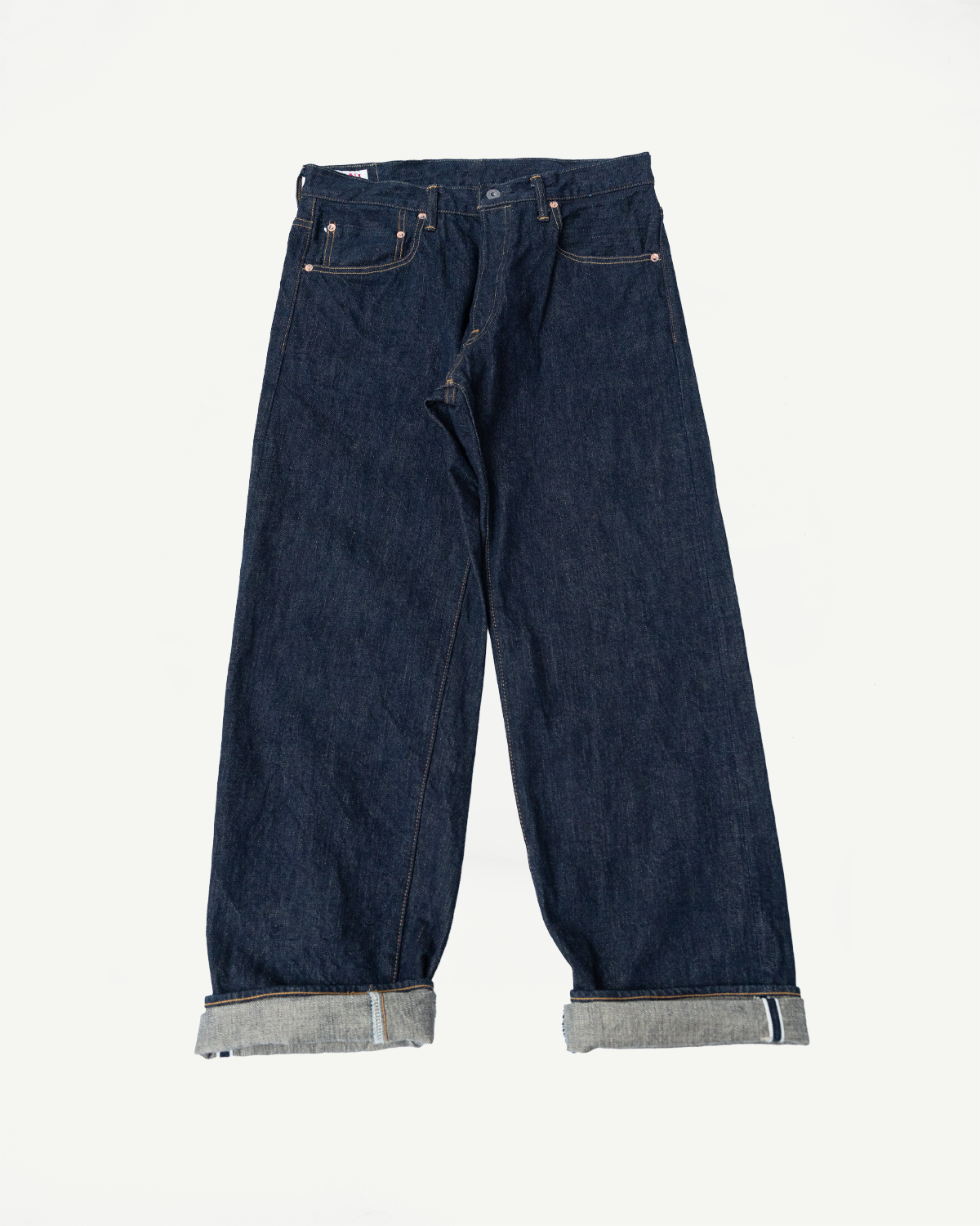 Front view flat lay of dark selvedge denim jeans with cuffed hems showing selvedge edge, copper rivets, and classic stitching.