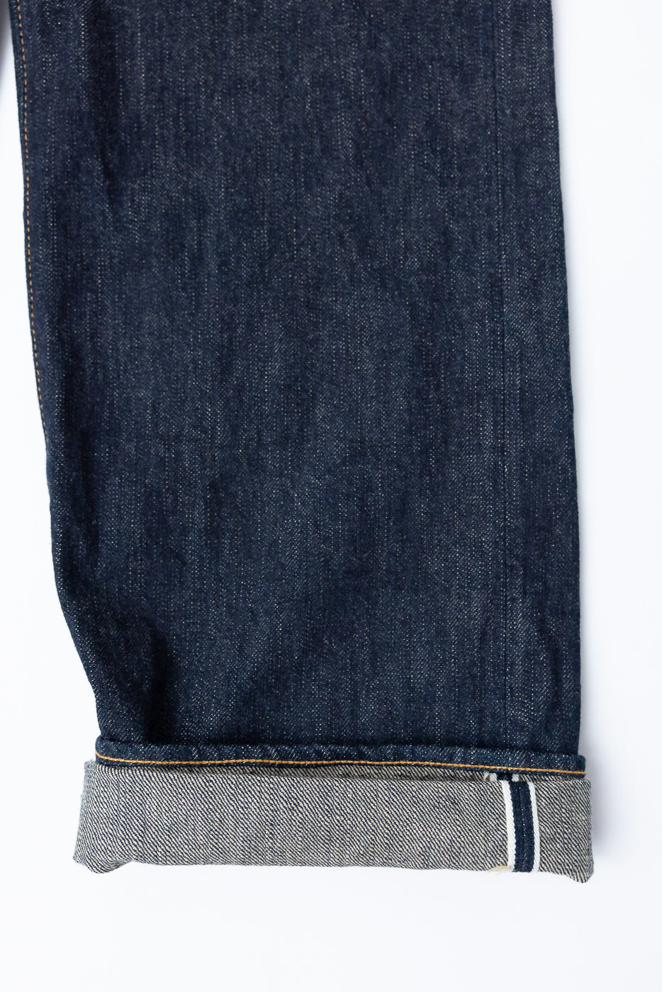 Close-up front view of selvedge denim jeans leg, showcasing raw hem, contrast stitching, and selvedge edge detail
