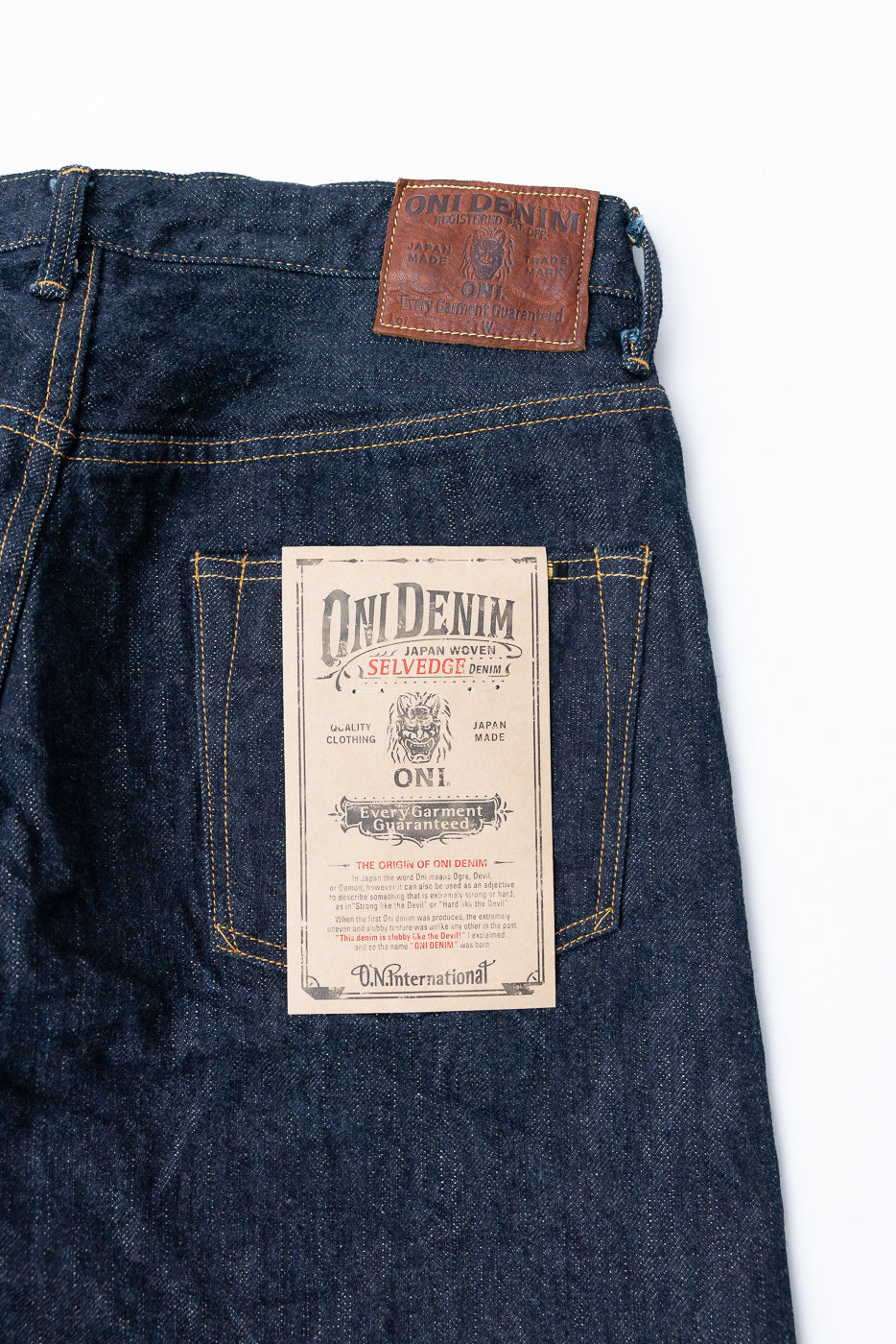 Close-up back view of Oni Denim selvedge jeans showing leather patch & paper tag, Japan-made, with yellow stitching