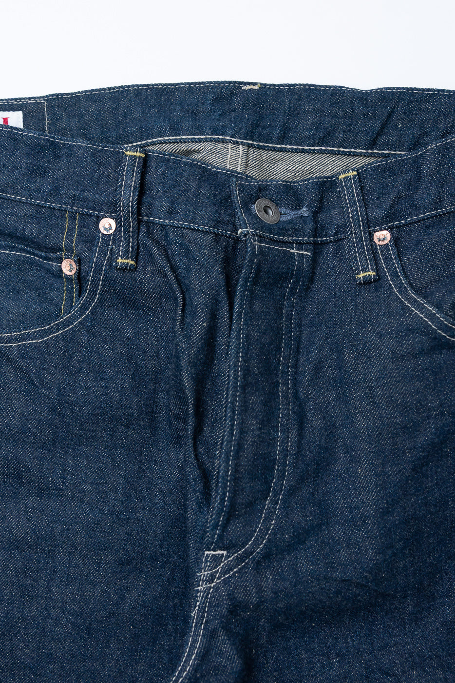Close-up of front waist and fly of 15oz selvedge denim, showing button closure and pocket details.