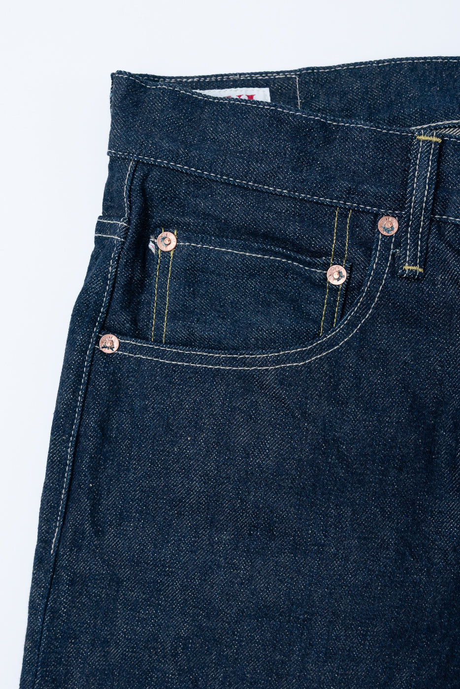 Close-up of front left pocket and coin pocket on selvedge denim jeans, showing brass rivets and heavy-duty stitching.