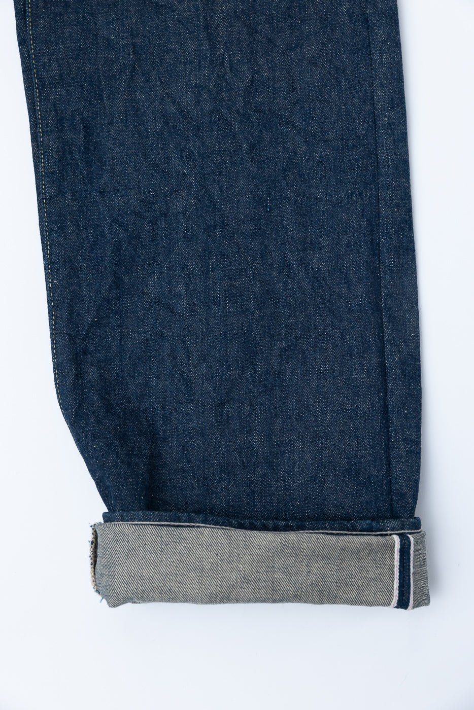 Close-up of denim pant leg front, showing cuffed hem and selvedge edge details.