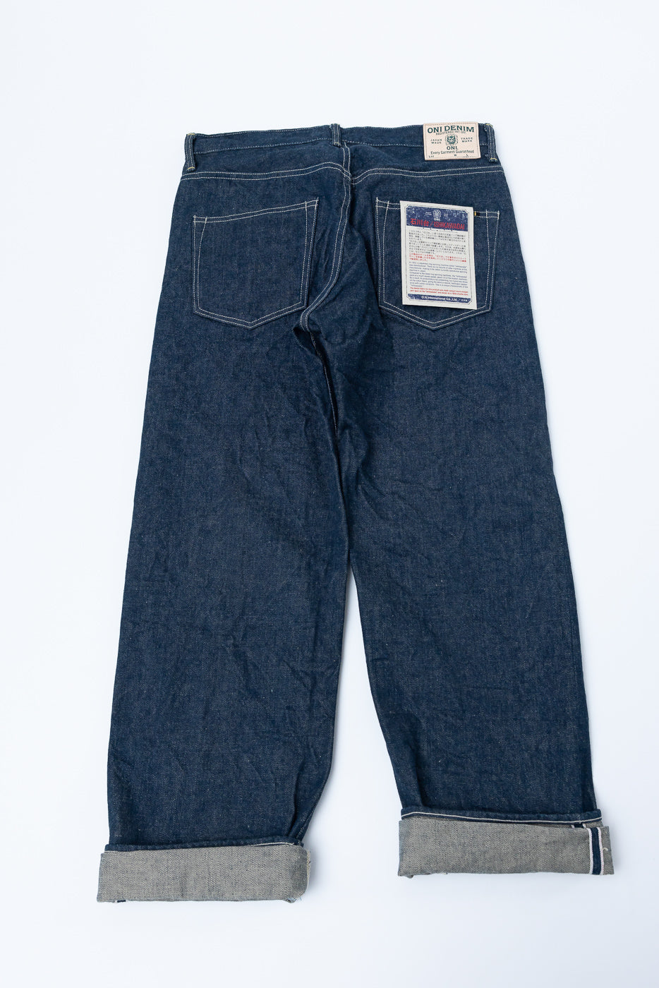 Flat lay of back side of wide straight selvedge denim jeans, showing labels, patch, and pockets.