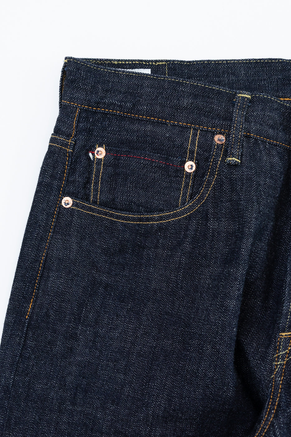 Close-up front view of dark selvedge denim jeans, showcasing copper rivets, yellow stitching, and raw fabric texture.