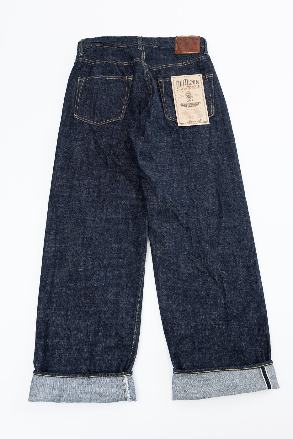 Back view flat lay of dark raw selvedge denim jeans with cuffed hems, back pockets, and ONI Denim label.