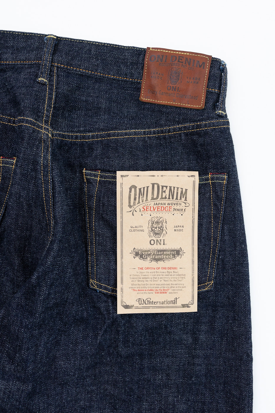 Close-up back view of dark selvedge denim jeans showing ONI Denim leather patch and paper tag, Japan-made, with yellow stitching detail