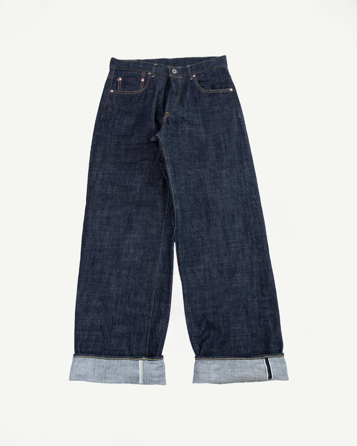 Front view flat lay of dark selvedge denim jeans with cuffed hems showing raw edge and contrast stitching