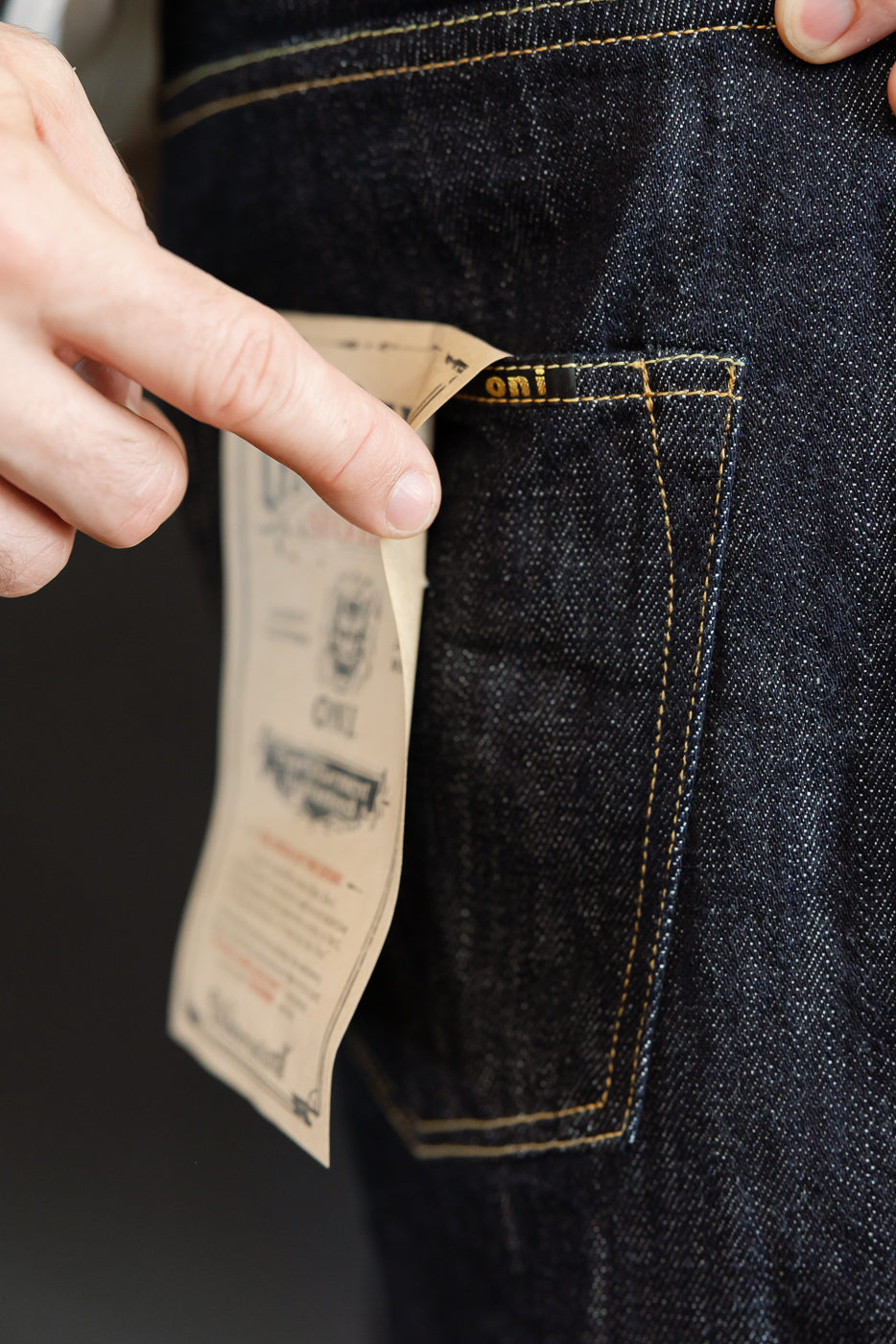 Close-up of dark selvedge denim jeans front pocket, showing tag details and gold stitching