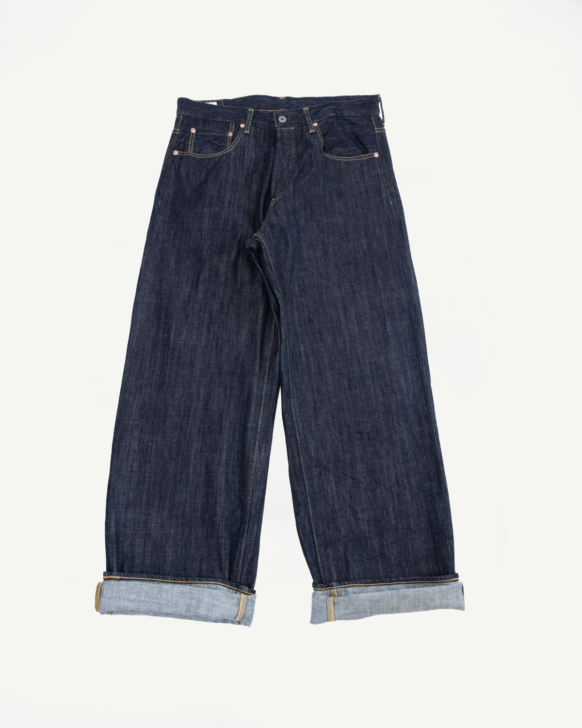 Front view flat lay of dark selvedge denim jeans with wide legs, cuffed hems showing lighter interior, and copper rivets.