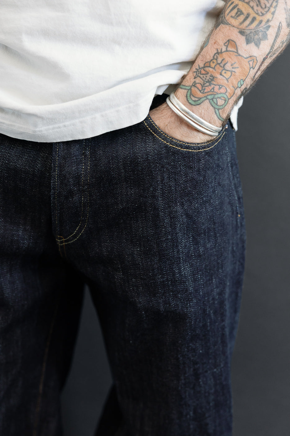 Close-up front view of dark selvedge denim jeans, male model with tattooed arm, athletic build