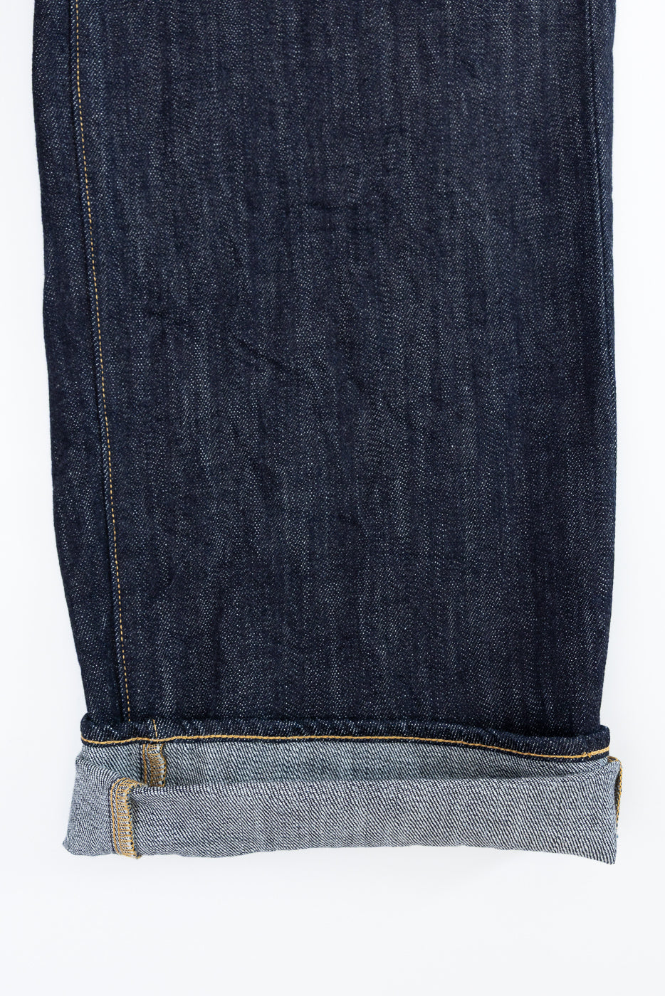 Close-up of dark selvedge denim jeans leg, front view, showing raw hem with contrast stitching and fabric texture