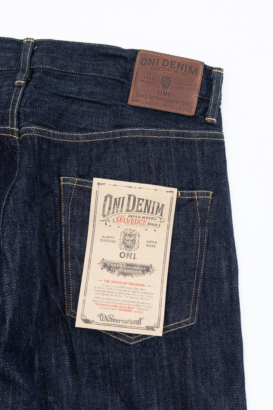 Close-up front view of Oni Denim selvedge jeans, showing leather waist label and paper back pocket tag, Japan-made