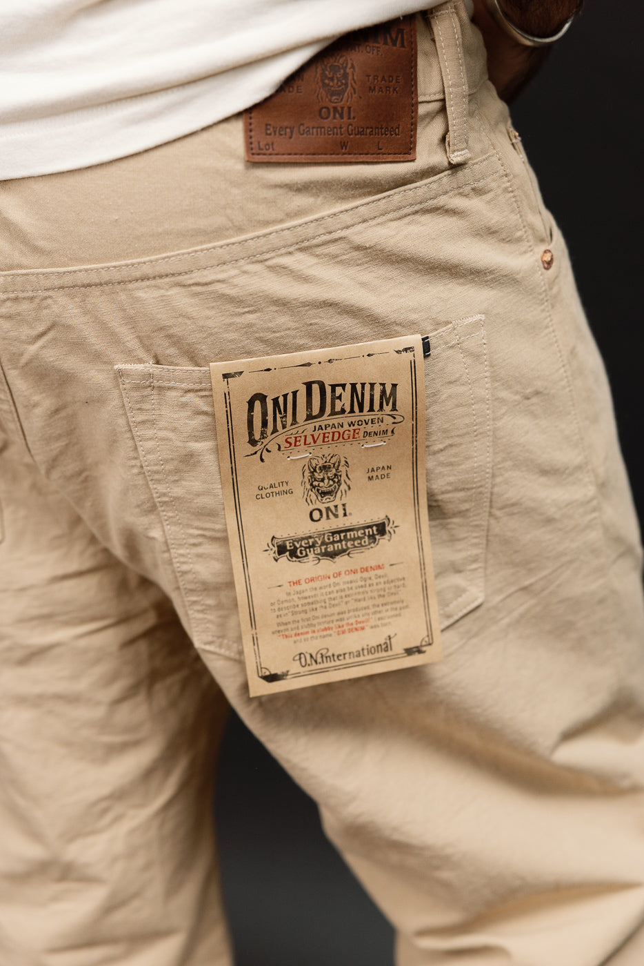 Close-up back view of male model wearing beige selvedge denim pants, showing ONI Denim tag and leather waist label