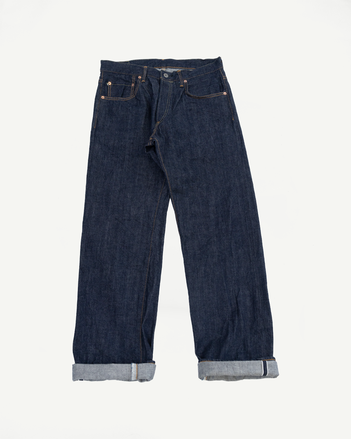Full body front view of dark indigo selvedge denim jeans with cuffed hems.