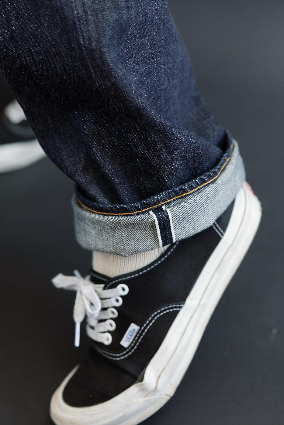 Close-up of the hem of dark indigo selvedge denim jeans worn by a male model.