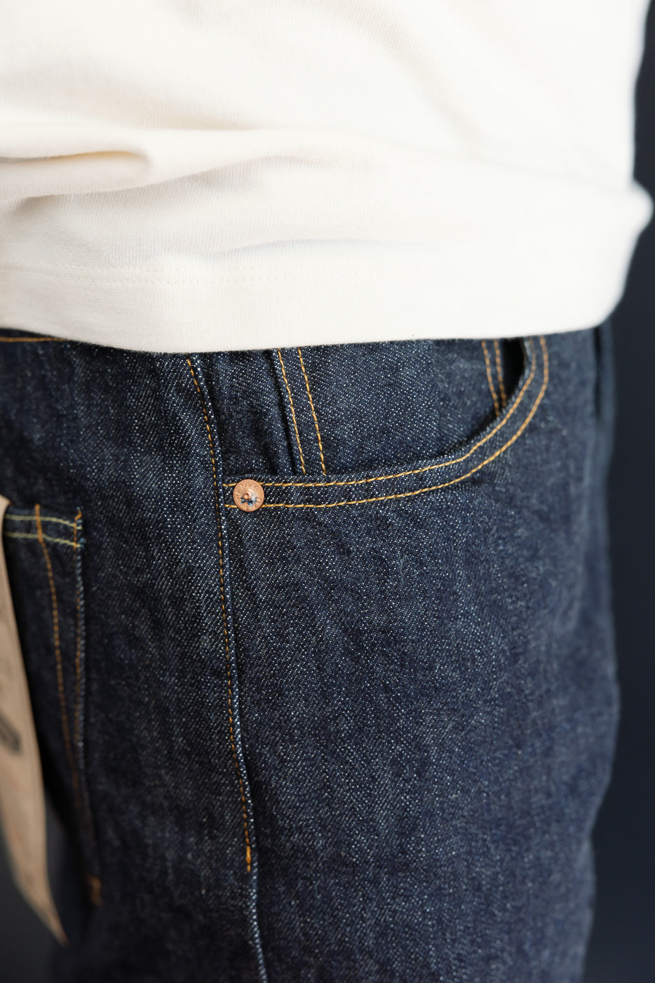 Close-up of front right pocket and copper rivet on dark selvedge denim worn by a male model.