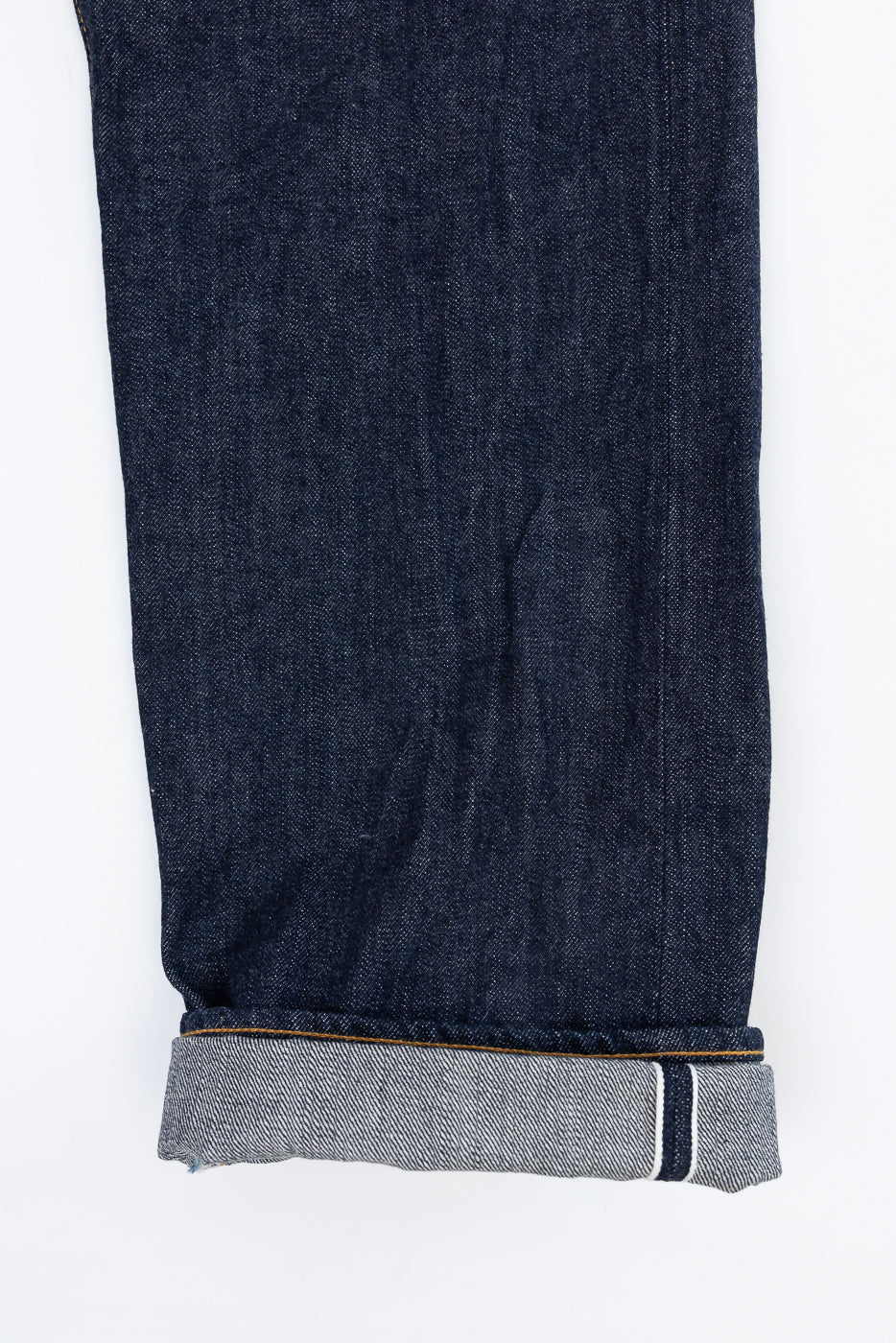 Close-up flat lay of the bottom hem and selvedge edge of dark indigo denim jeans.