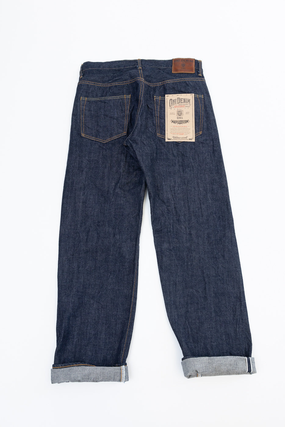 Back view flat lay of Oni Denim dark indigo selvedge jeans with brand tag and leather patch.