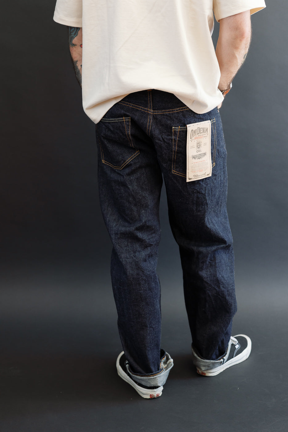 Back view of male model in dark selvedge denim jeans, showing the rear pocket and brand tag.