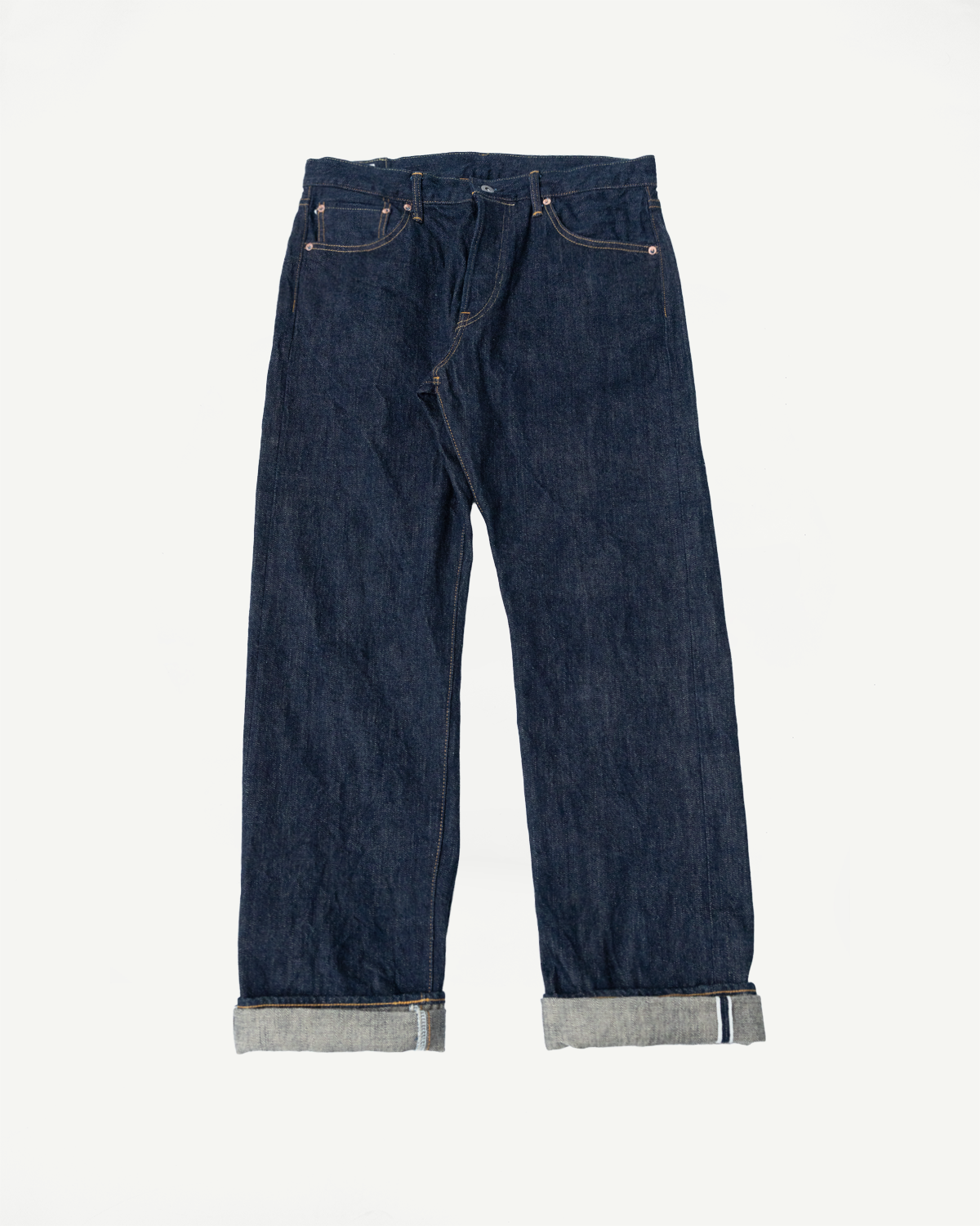 Front flat lay of dark selvedge denim jeans with cuffed hems showing selvedge ID stripe, gold stitching, and classic 5-pocket design.