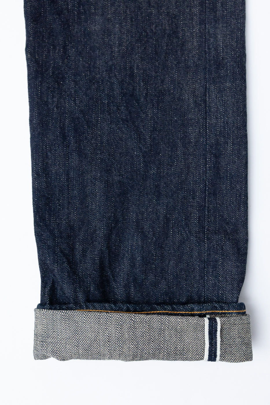 Close-up of selvedge denim jeans hem, showing raw edge, contrast stitching, and signature selvedge stripe detail
