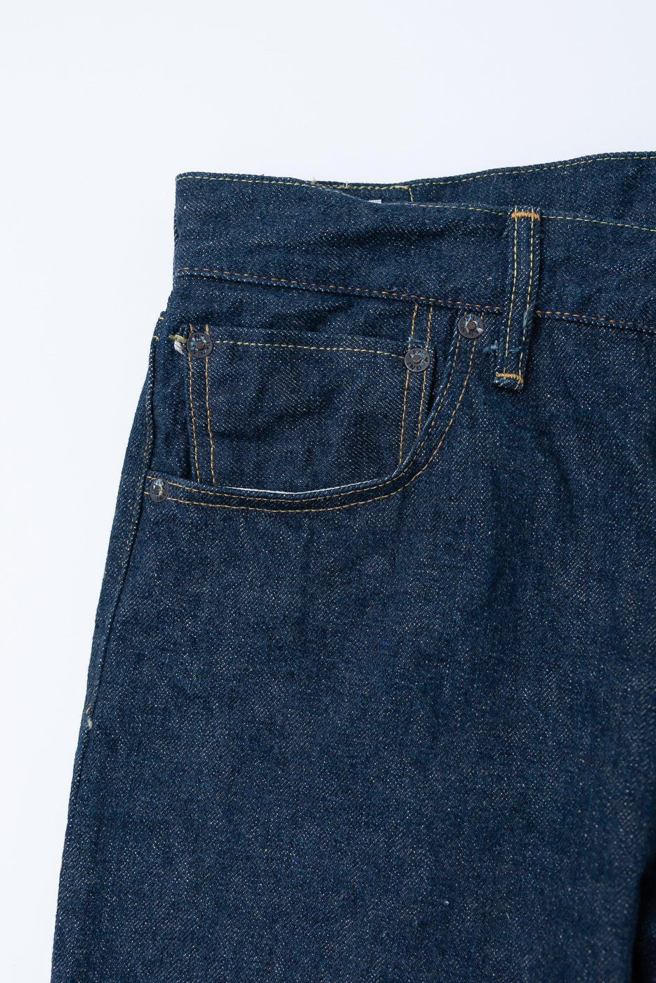 Close-up of front left pocket and waistband on 15oz selvedge denim jeans, showing metal rivets, belt loop, and textured indigo fabric.