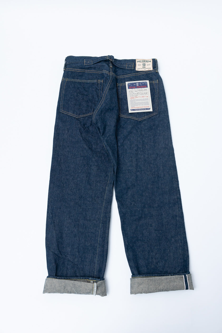 Flat lay of back side of loose straight 15oz selvedge denim jeans with cinch back, visible back pockets, patch tags, and cuffed hems.