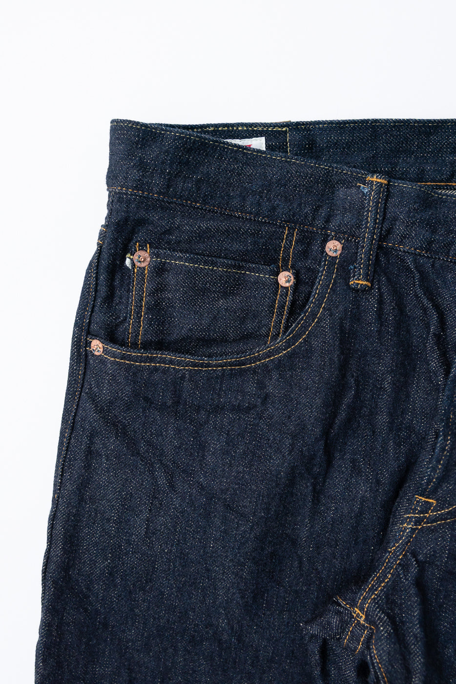 Close-up front view of dark selvedge denim jeans with copper rivets and yellow stitching detail