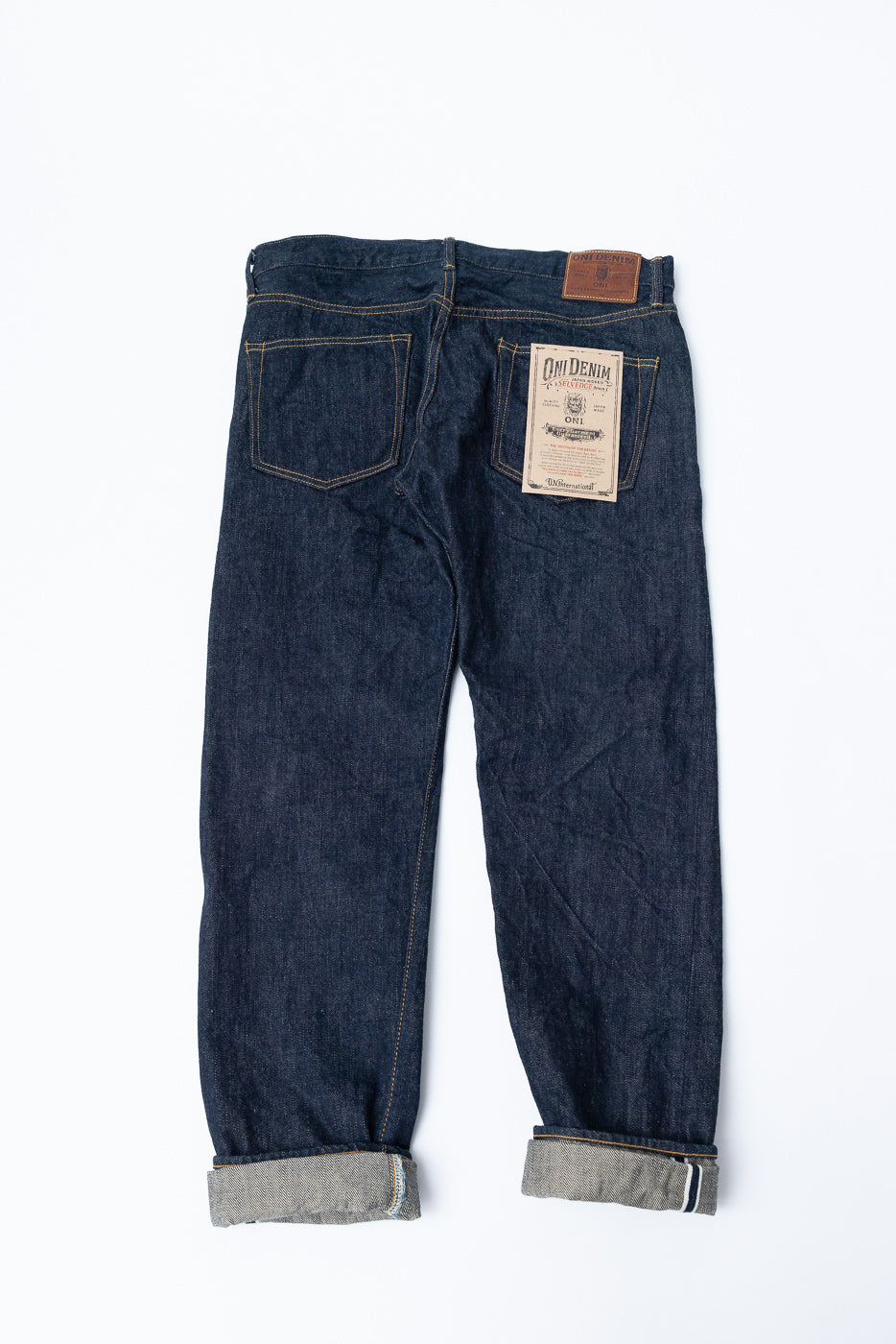 Back view of selvedge denim jeans with cuffed hems, showcasing back pockets and brand patch.