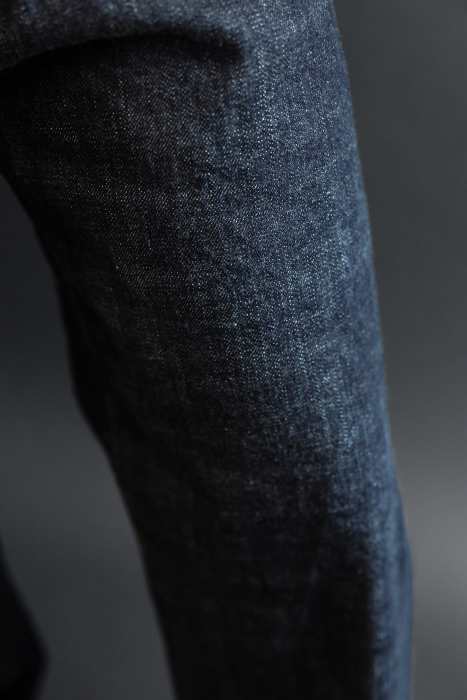 Close-up of dark selvedge denim jeans leg, showcasing fabric texture and weave detail on male model