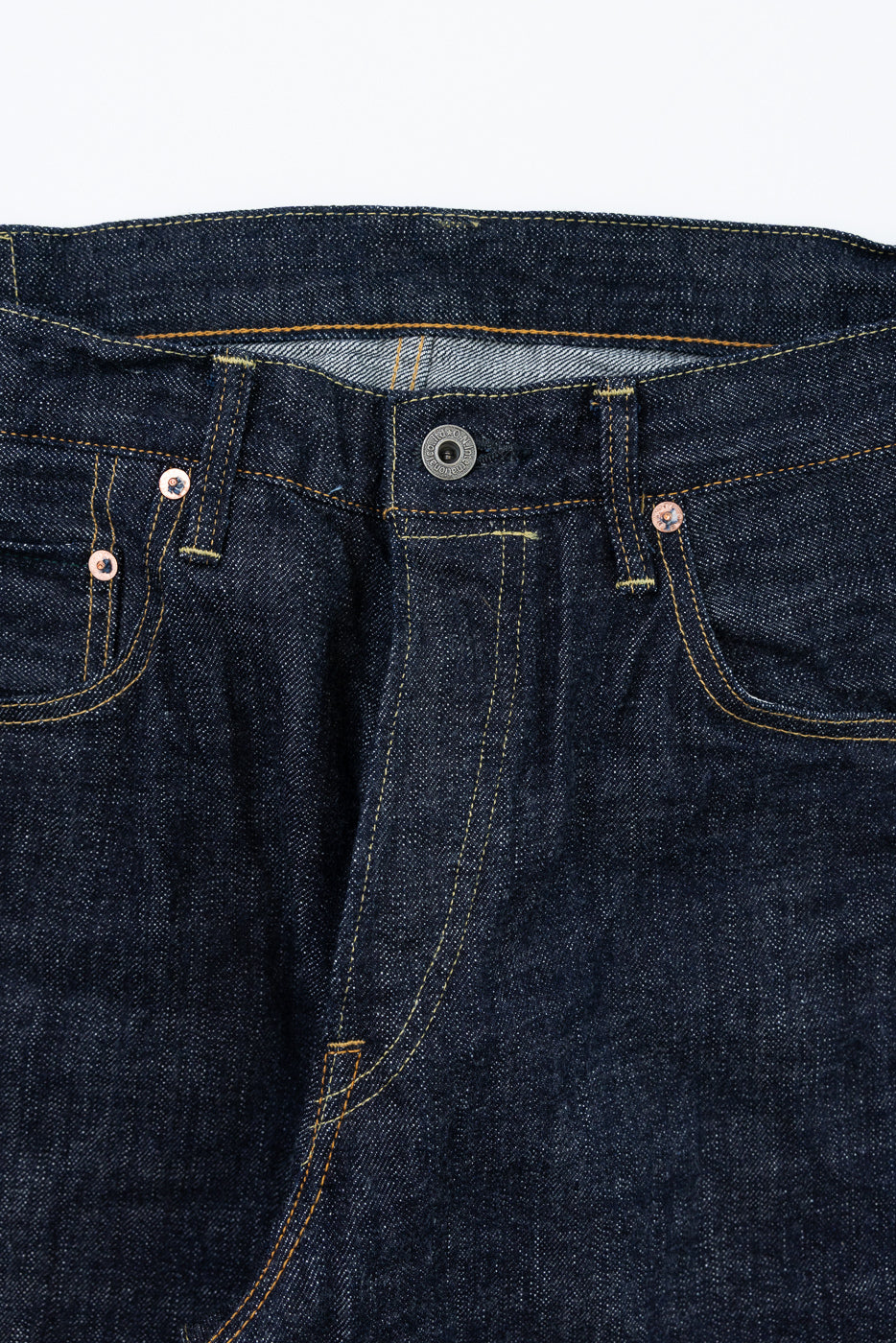 Close-up front view of dark selvedge denim jeans showing button fly, copper rivets, and contrast stitching