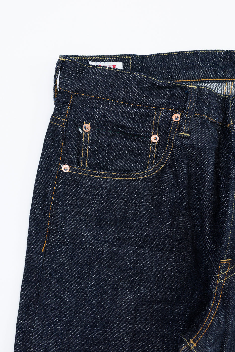 Close-up front view of dark selvedge denim jeans with copper rivets and yellow stitching detail