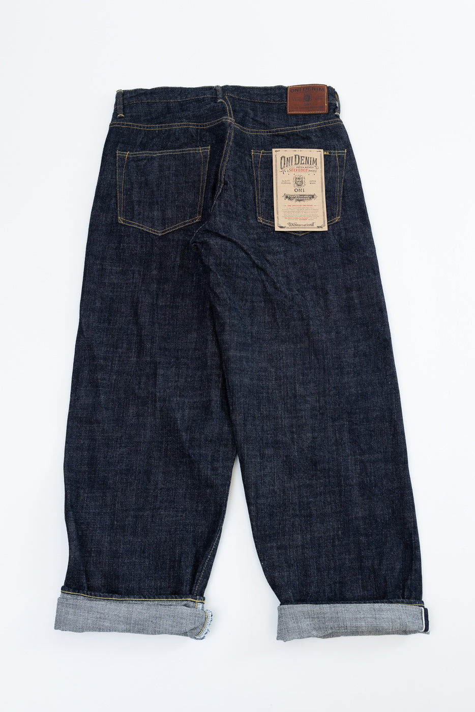 Back view flat lay of dark selvedge denim jeans with cuffed hems, back pockets, and ONI Denim label