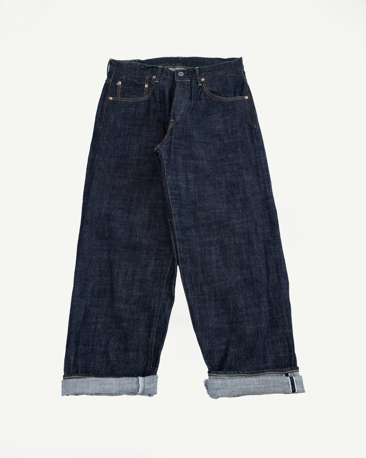 Front view flat lay of dark raw denim jeans with cuffed hems, copper rivets, and selvedge detail visible on rolled cuffs