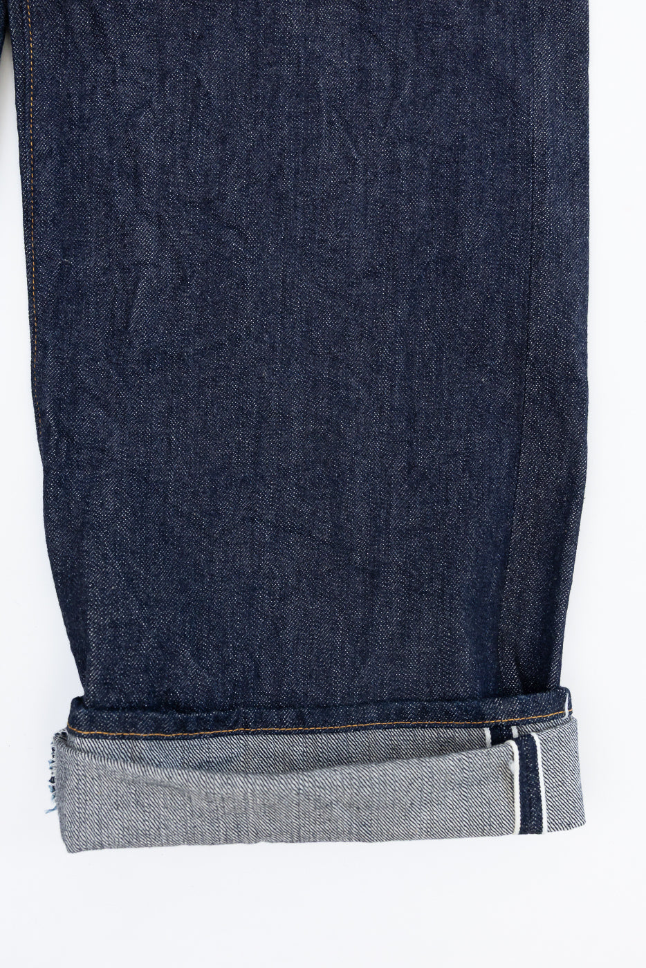 Close-up front view of dark indigo selvedge denim jeans cuff showing white edge detail.