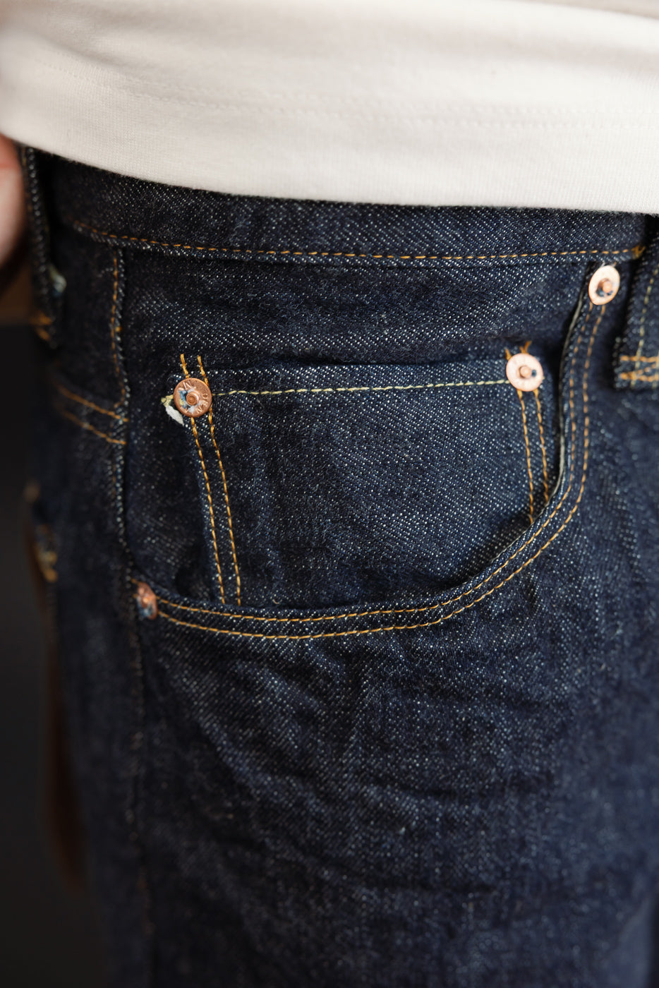 Close-up of the back pocket of dark indigo selvedge denim jeans showing fabric texture and stitching.