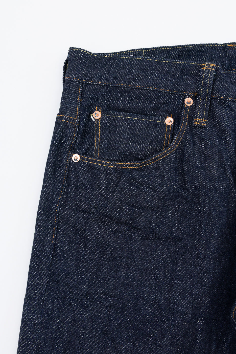 Close-up front view of dark indigo selvedge denim jeans showing pocket and rivet details.