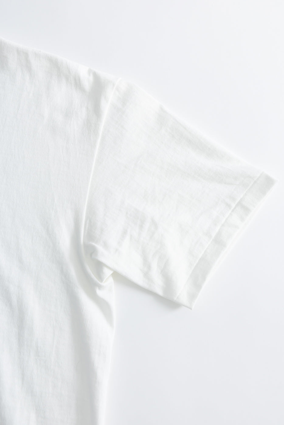 Close-up of a white T-shirt, flat lay, showing left sleeve and side seam details.