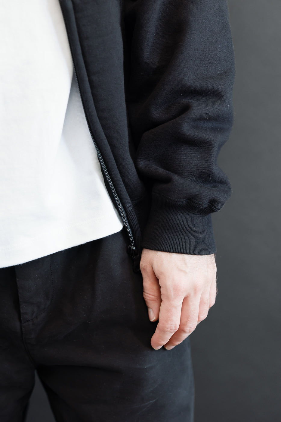 Close-up of the side and front of a male model's black zip-up hoodie and white t-shirt.