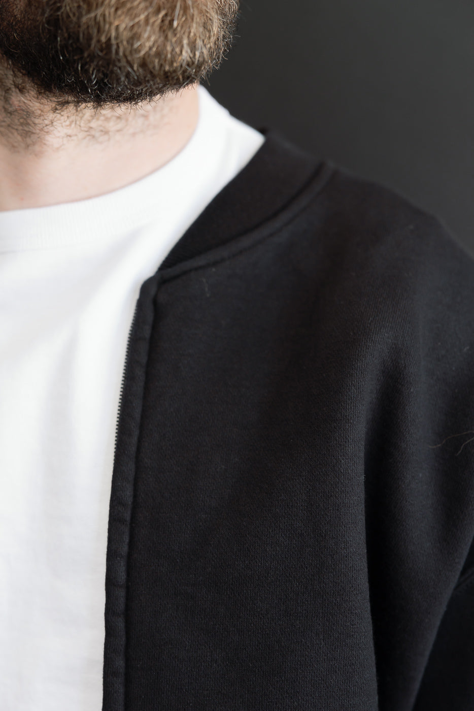 Close-up front view of a male model wearing a black bomber jacket over a white t-shirt.