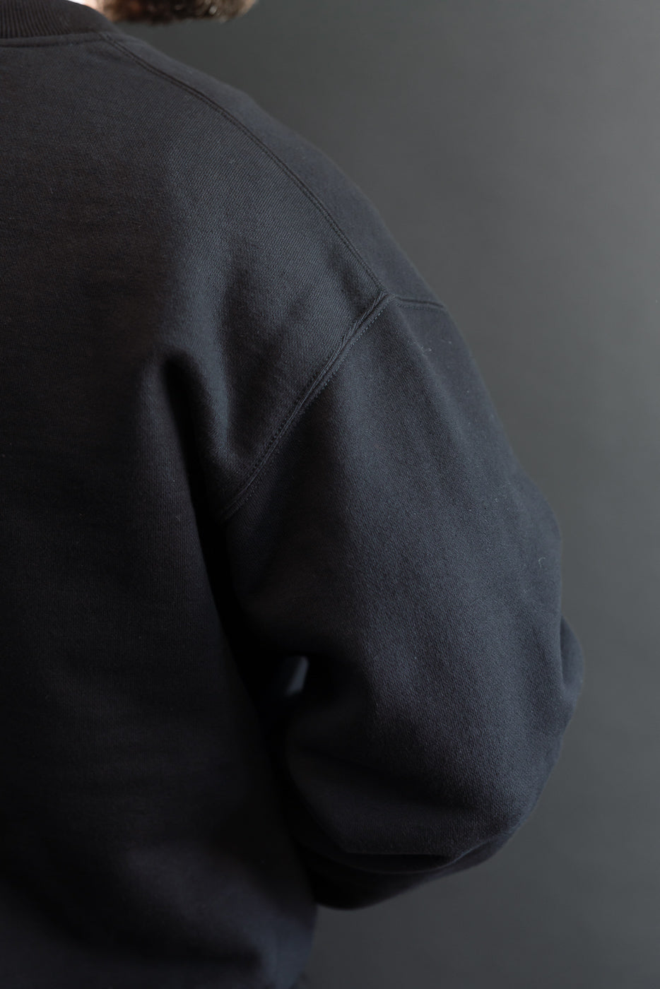 Close-up view of the back and side of a black crewneck sweatshirt showing fabric texture.