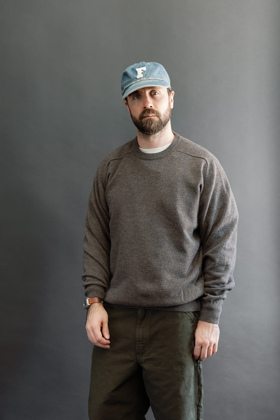 Front view, full body shot of a male model with an athletic build wearing a brown crewneck sweatshirt and olive trousers.